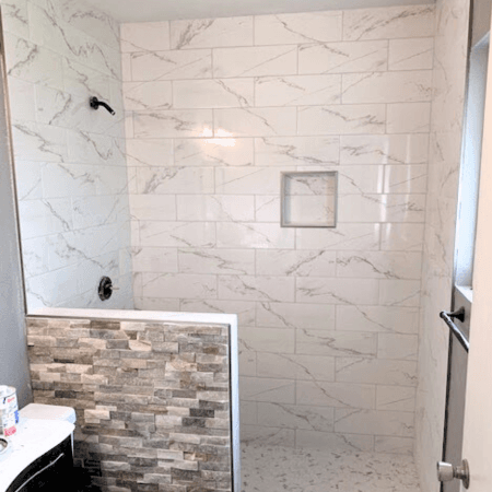 Modern granite tile bathroom with a stacked stone tile accent wall separating the shower and toilet