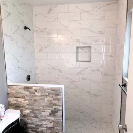 Modern granite tile bathroom with a stacked stone tile accent wall separating the shower and toilet