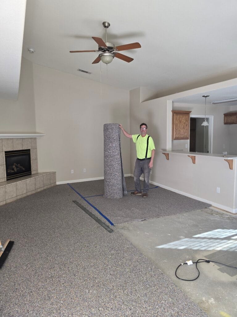 Walt standing in a living room leaning on a carpet roll during a residential carpet install