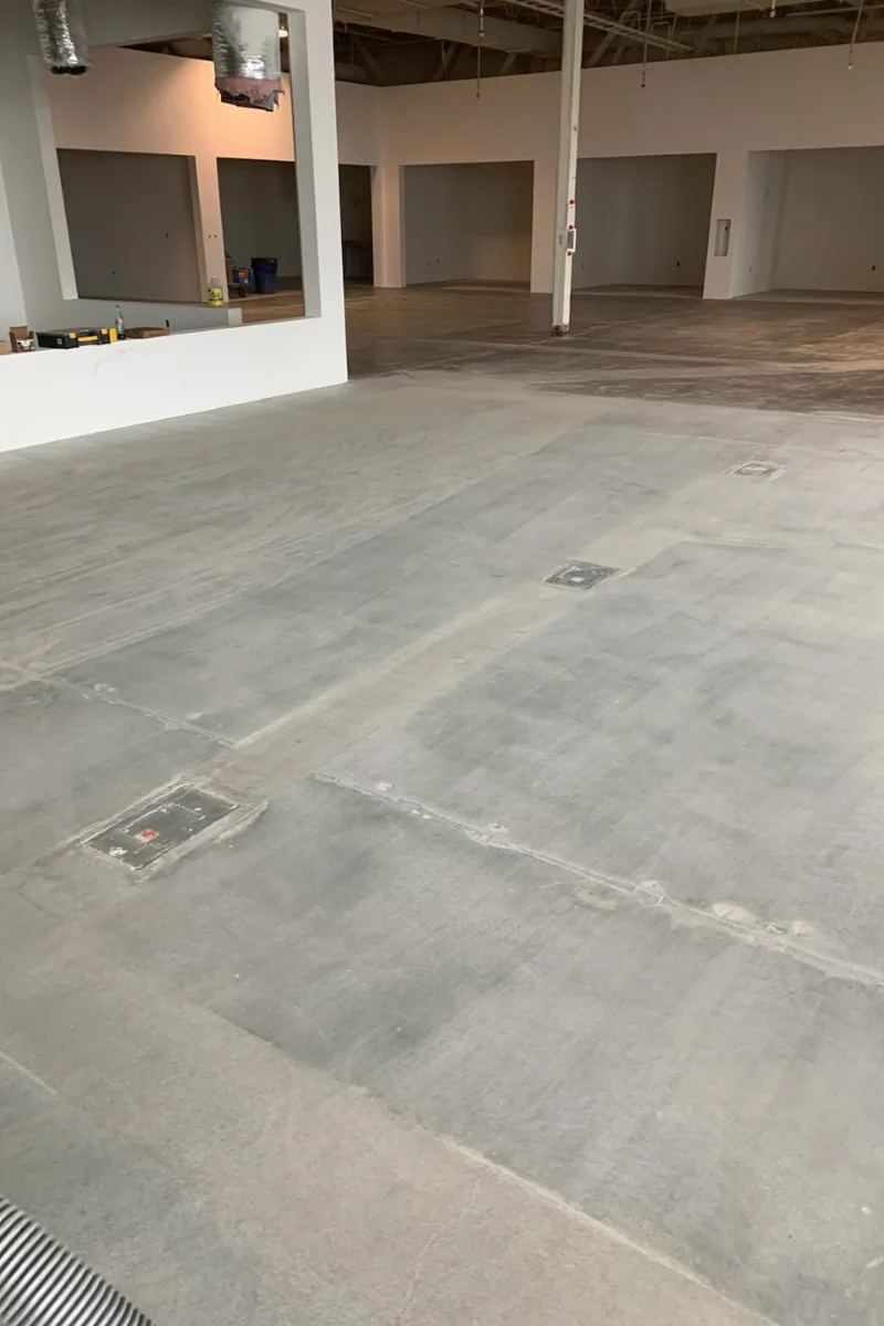 Empty unfinished showroom/warehouse interior with concrete floor, white walls, and exposed ducts.