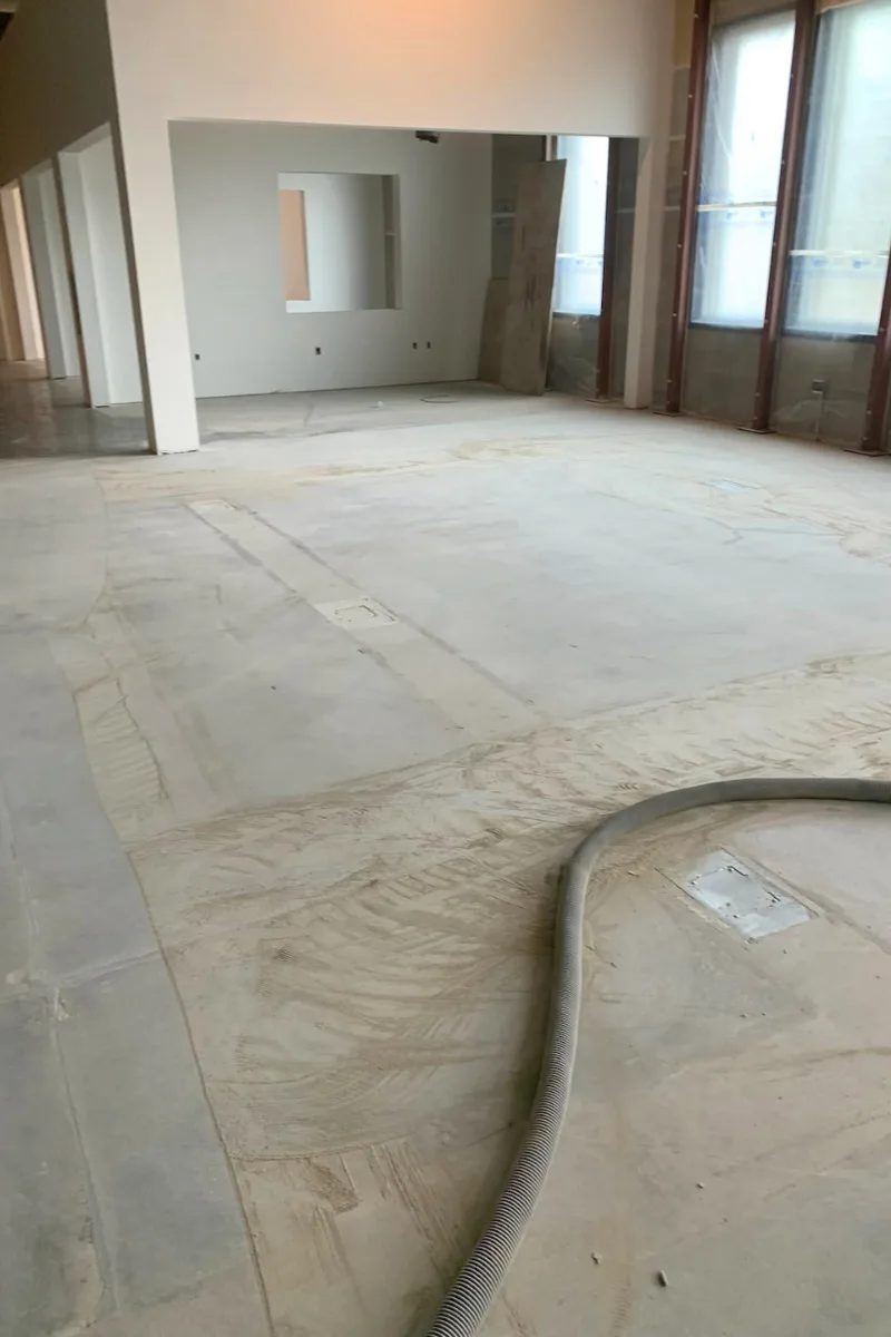 Empty commercial space under renovation with a dusty concrete floor and a flexible hose snaking across the area.