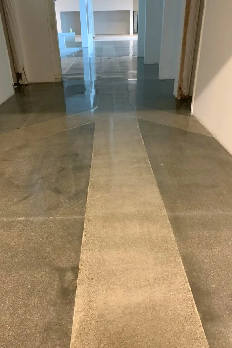 Empty hallway with a glossy, reflective floor; a pale central stripe runs down the middle of the walkway, flanked by darker floor surfaces.