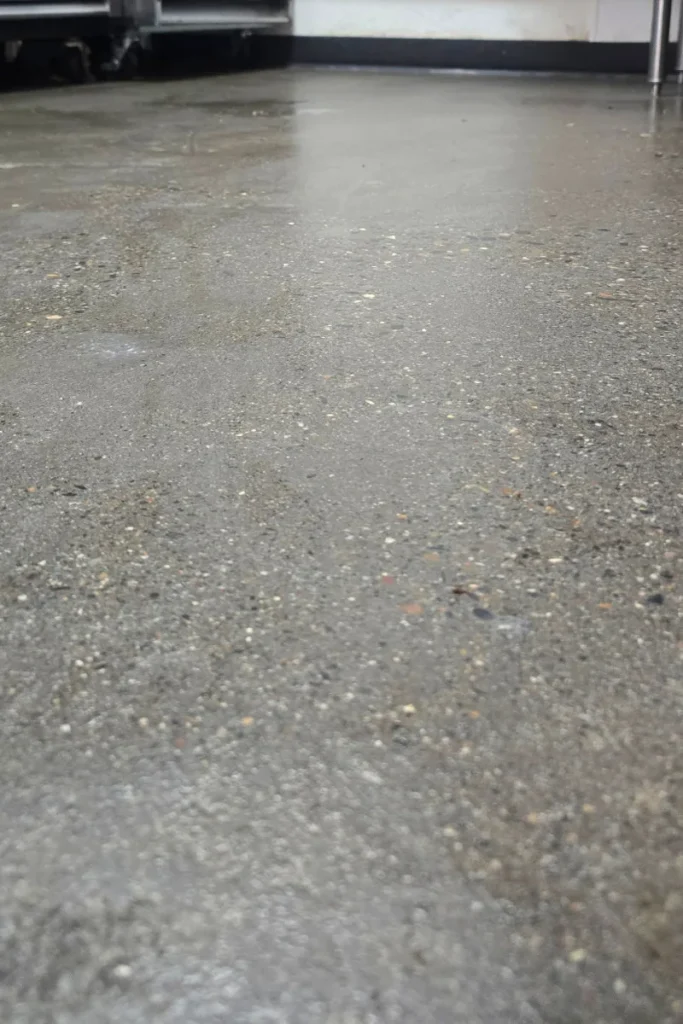Wet concrete floor with reflections, indoors near walls and furniture legs visible at the top edge